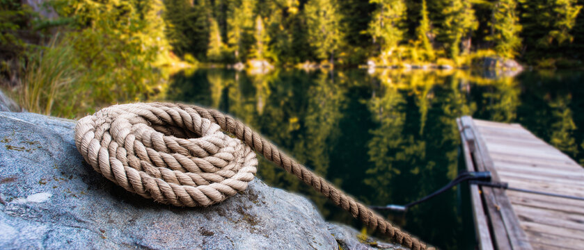 Corda enrolada sobre pedra ao lado de lago com floresta ao fundo representando tranquilidade, natureza e ambiente ao ar livre, conceito de descanso e paisagem natural
