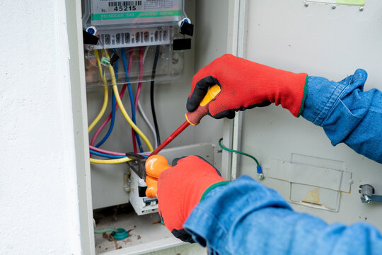 Close-up of an electrician's hands using pliers and a screwdriver to install and maintain an electric meter