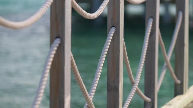 Wooden railing with twisted ropes by turquoise water, detail tropical marine shot