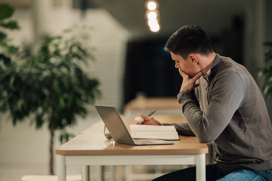 Man seriously thinking while working on laptop and writing notes