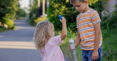 Fototapeta premium Brother and sister playing with soap bubbles on a country road in summer.