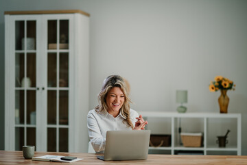 Woman smiling and laughing during video call or online meeting using a laptop at home office desk,...