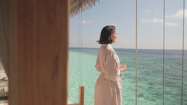 Woman on overwater bungalow overlooking turquoise sea