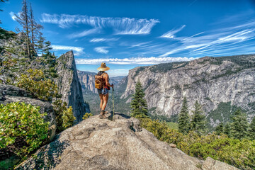 A woman is standing on a mountain top, looking out over the landscape