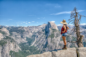 A woman wearing a straw hat stands on a mountain top © ExploringandLiving