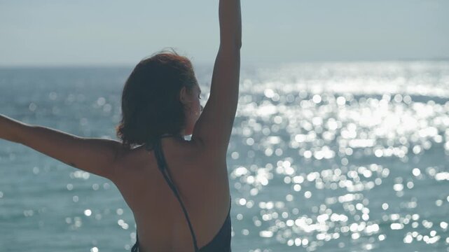Woman at ocean edge with sparkling water stretching with light yoga moves, enjoying the environment on an island in the Maldives