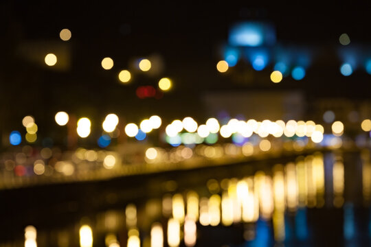 Luces urbanas nocturnas con efecto bokeh y reflejos.Luces de ciudad desenfocadas reflejadas en el agua durante la noche, creando un efecto bokeh colorido con tonos c&aacute;lidos y fr&iacute;os. Escena urbana atmos