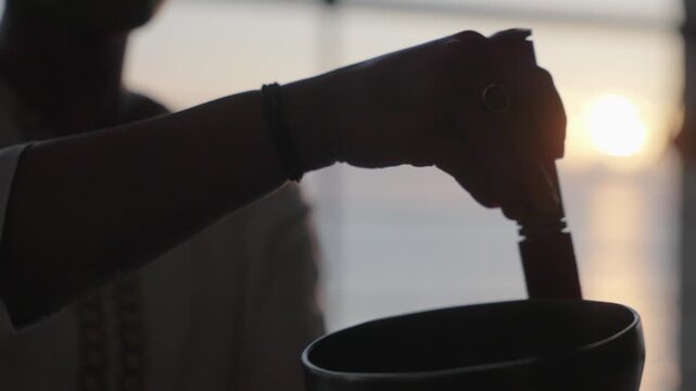 Silhouette of hands ringing a singing bowl at sunrise at a pavilion overlooking the ocean