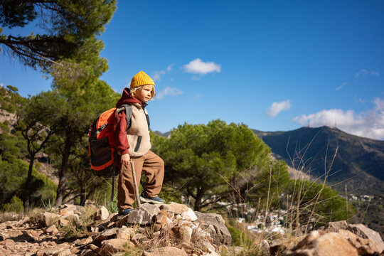 Focused young boy hiking on mountain trail, standing on rock with backpack, exploring nature independently, outdoor adventure, childhood freedom, travel experience and confidence development