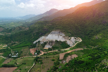 Fototapeta premium Aerial view shows a quarry on a hillside in Southeast Asia where large blocks of stone are being extracted and moved by machinery. Heavy equipment is also visible