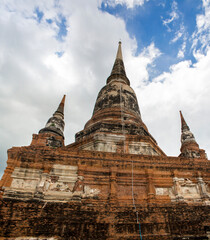 Fototapeta premium A low-angle, monumental perspective looking up at the weathered spires of a grand Siamese chedi. Ruins of the Wat Yai Chai Mongkhon located in the Ayutthaya Historic Site, Thailand. 