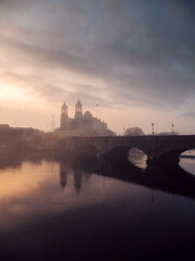 Fototapeta premium View on Athlone town bridge at sunset. Cloudy warm orange sky. Popular old city in Ireland. Educational, tourist and industrial center.