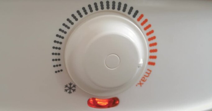 Regulator for heating water in home boiler. Man turns temperature control on heater of water. Red light indicator comes off, boiler has turned off. Boiler heats water from cold water supply system
