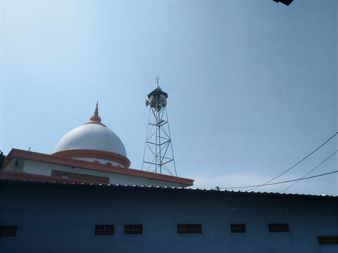 Kubah Masjid dengan menara pengera suara latar belakang langit biru.