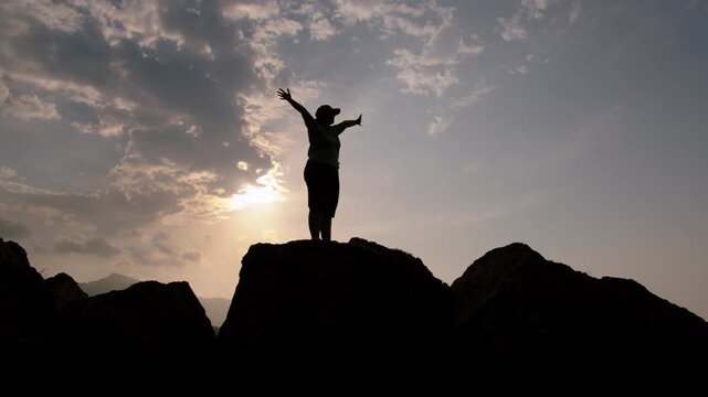 Woman Standing on Mountain at Sunset with Raised Arms Enjoying Breathtaking Scenic View