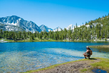 A woman is sitting by a lake, looking out at the mountains in the distance