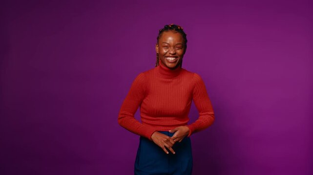 Amused young woman laughs heartily and covers her mouth with her hand. Studio shot with a purple background.