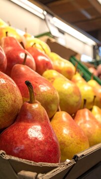 Pile of reddish-yellow pears, displayed in boxes under indoor lighting