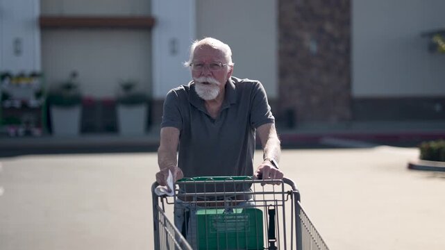Senior man moves grocery cart across parking lot to reach his car after completing shopping at the grocery store
