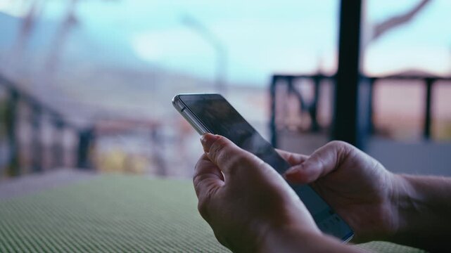 Hands of Woman Typing on Smartphone Outdoors at Terrace Overlooking Mountains