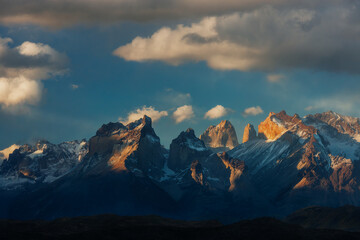Obraz premium Majestic granite peaks of the Cuernos del Paine at sunset with golden light hitting the mountain tops under a dramatic sky in Patagonia, Chile.