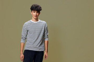 young man wearing a striped shirt standing against a plain olive background, casual style with...