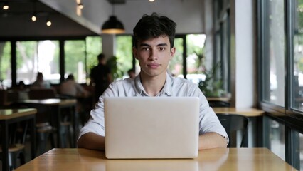 Young hispanic male working on laptop in modern cafe.
