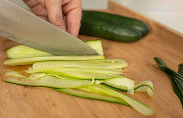 Slicing cucumbers with a large knife on wood cooking board close-up