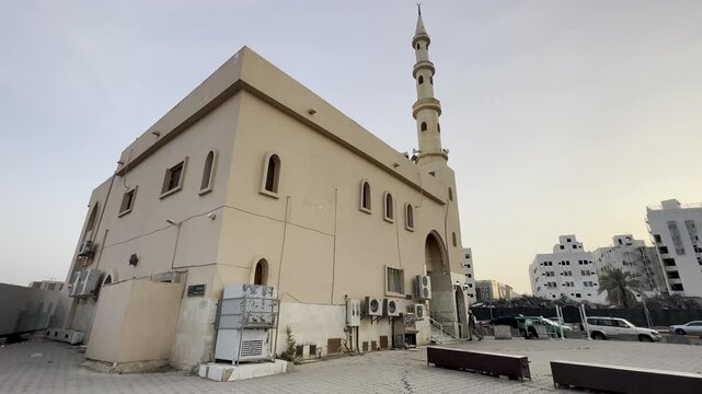 A clear exterior view of the historic Abu Zar Ghafari Mosque (Masjid Abu Dharr al-Ghifari) in Medina, highlighting its traditional minaret and stone facade against a bright sky.
