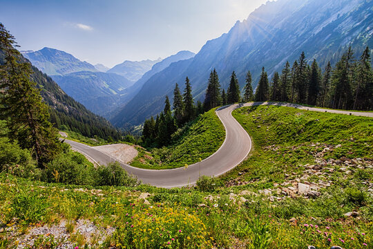 Scenic mountain road with sharp curve surrounded by lush green slopes and dramatic alpine peaks along Silvretta Bielerhohe road.