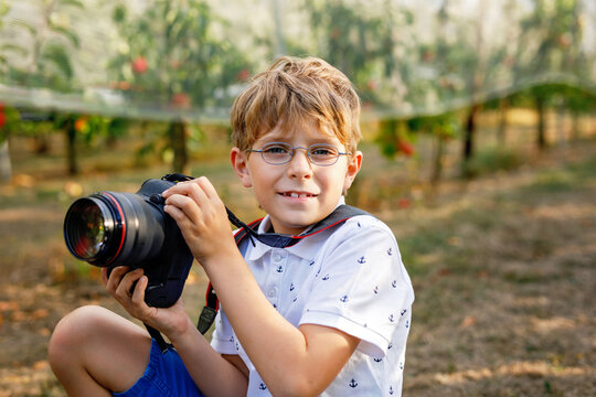 Young boy taking photos with a DSLR camera in an apple orchard, sitting outdoors during harvest season, creative hobby and real life childhood moment.