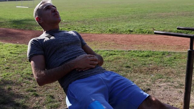 54-Year-Old Fit Man in Excellent Physical Condition Doing Crunches on Parallel Bars.  Athletic Middle Aged Man Doing Sit-ups. Series Track Code: Fit-Mature-Man-54-Outdoor-Fitness-Series-2024