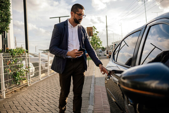 Urban professional using smartphone to request or access ride hailing transportation beside a parked car in a modern city environment, representing app mobility and daily commuting.