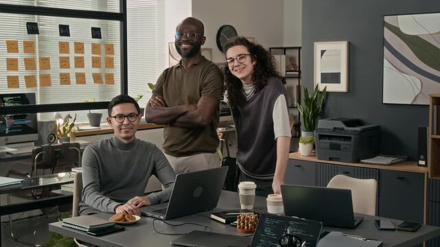 Group portrait of three cheerful young male programmers looking at camera during workday in modern office of IT company