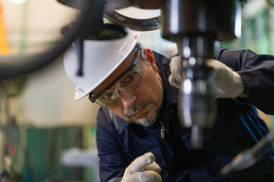Professional technician checking industrial drill machine precision manufacturing factory. Metalworking engineer wearing safety helmet glasses operating heavy equipment mechanical maintenance workshop