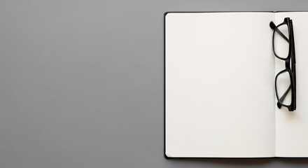 Open blank notebook on gray surface with black framed glasses placed on pages conceptualizing knowledge learning and business or medical research idea