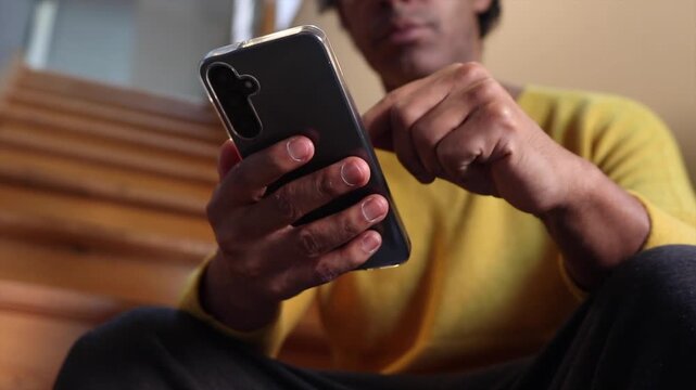 Man using smartphone for texting, browsing social media, and online communication while sitting on stairs at home