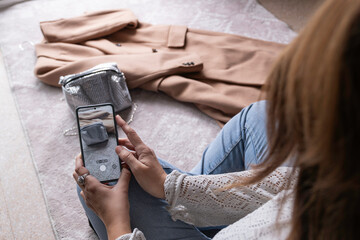 An anonymous woman taking photos of secondhand clothes with her mobile phone to sell online in a thrift store