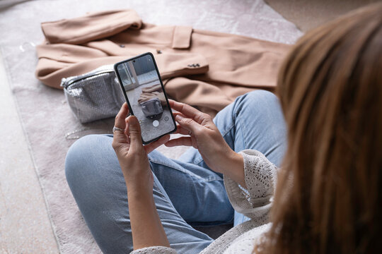 An anonymous woman taking photos of secondhand clothes with her mobile phone to sell online in a thrift store