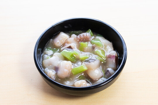 Japanese Tako Wasabi, raw octopus seasoned with wasabi and herbs in a black bowl, served as an appetizer on a light wooden background.
