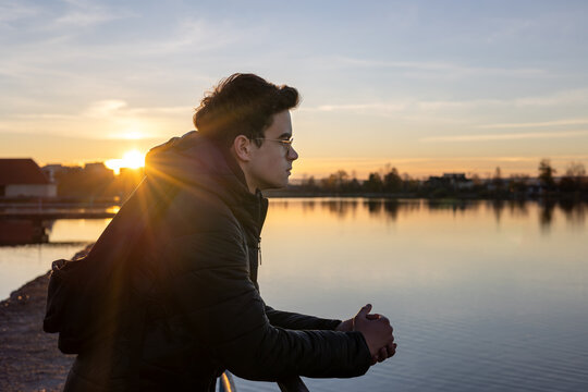 Teenage boy sitting outdoors near water at sunset, looking thoughtful. Concept of adolescence, self-reflection, emotional development, mental health, identity search and transition to adulthood.
