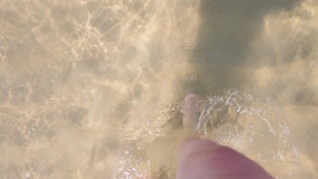 Woman's bare feet on the beach, creating ripples on the surface of the water