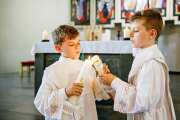 Two little kids boys receiving his first holy communion. Happy children holding Christening candle....
