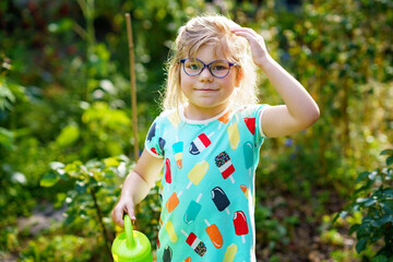 Little girl in a garden with green watering pot. Preschool child using rainwater to water flowers and plants. © Irina Schmidt