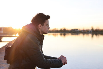 Teenage boy sitting outdoors near water at sunset, looking thoughtful. Concept of adolescence, self-reflection, emotional development, mental health, identity search and transition to adulthood. © Светлана Мищенко