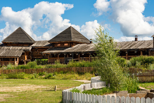 The impressive wooden walls of a reconstructed Old Slavic fortress, made of round, hewn logs. Old barracks and boyar chambers. A bright, sunny day.