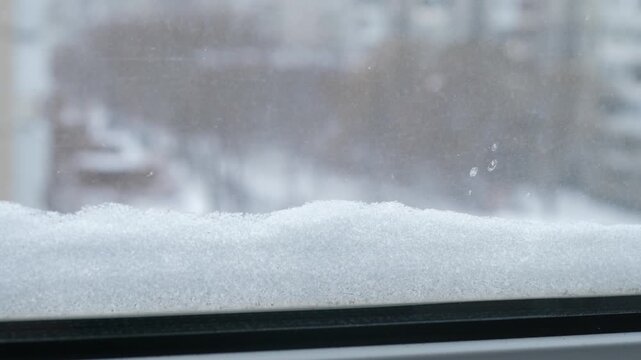 A thick layer of fresh snow lies on the outer window frame. View from the window of a snowy city during a winter snowfall