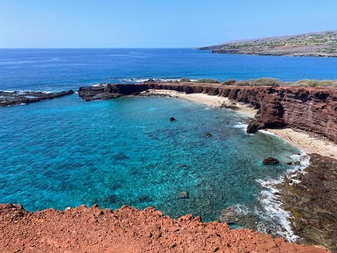 Turquoise waters and red lava cliffs frame Lana'i Cathedrals on Lanai, Hawaii, revealing a secluded cove beneath clear Pacific skies.