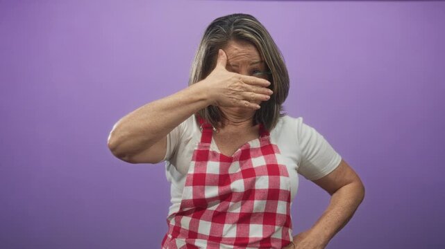 Woman cook in studio wearing red gingham apron covers face with hand in a privacy gesture, eyes hidden; embarrassment privacy.