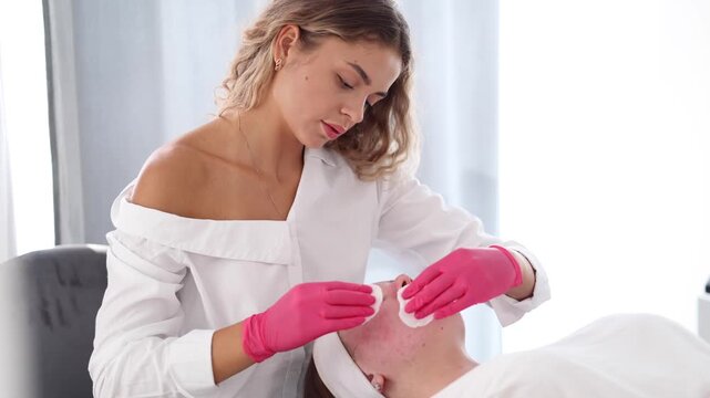 The beautician uses a hot pink glove to apply skincare treatment on the client, bringing a pop of color and uniqueness to the scene.